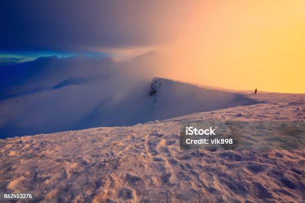 At The Edge Of The Snowy Rock Someone Is Standing The High Mountains In The Fog Morning Sky Is Enlighten With The Orange Colored Light In Winter Day Stock Photo - Download Image Now