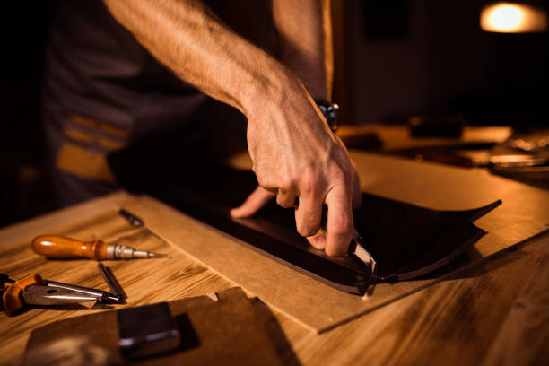 istock Working process of the leather belt in the leather workshop. Man holding crafting tool and working. Tanner in old tannery. Wooden table background 862454118