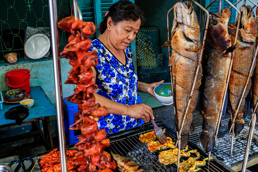 Vietnamese woman preparing grilled frogs and fishe, Mekong River Delta, Vietnam