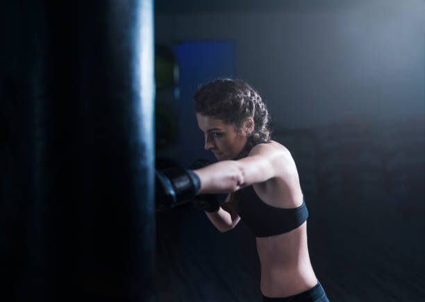 istock Young fighter boxer girl in training with heavy punching bag 862473472