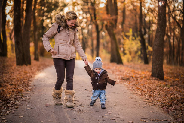 young mother is holding for hand her little son trout public park at autumn