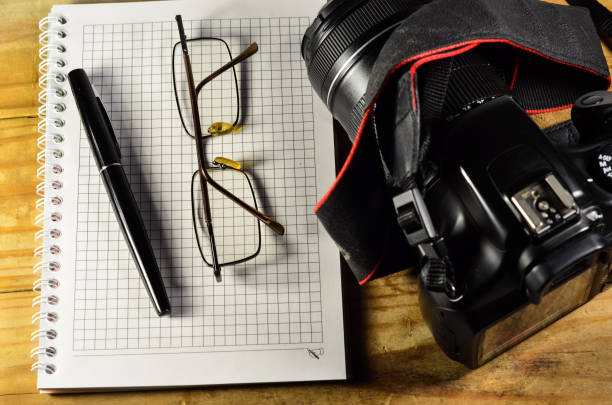 Fountain pen, modern camera, glasses, and notebook on a wooden table