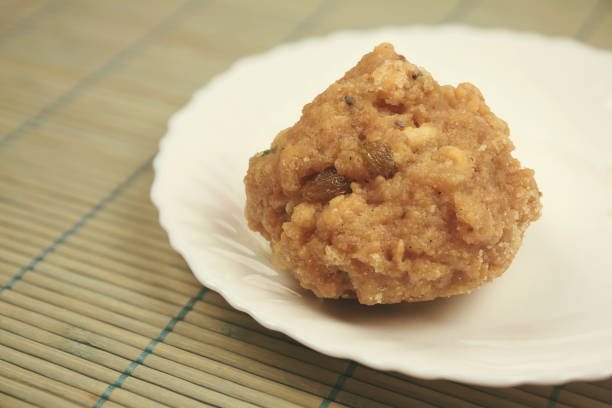 Close-up of golden, round Indian sweet treats (ladoo) placed inside a clear plastic jar, with a blurred and colorful shop background. The image evokes a warm, festive, and traditional Indian atmosphere.