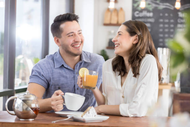 Young woman and young man on a first date Young couple on a first date enjoy spending time together in a local coffee shop. The woman is drinking a cup of hot tea. They are smiling and laughing together. blind date stock pictures, royalty-free photos & images