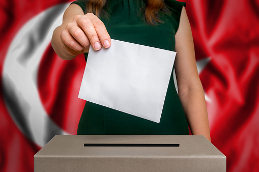 Election in Turkey - voting at the ballot box. The hand of woman putting her vote in the ballot box. Flag of Turkey on background.
