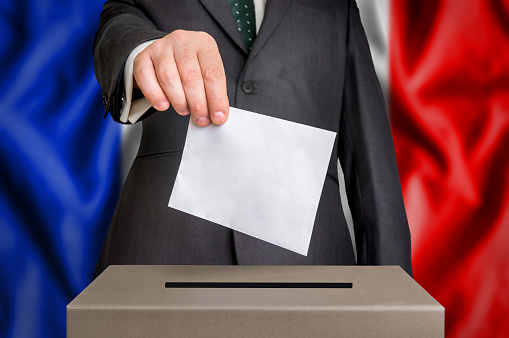 Election in France - voting at the ballot box. The hand of man putting his vote in the ballot box. Flag of  on background.