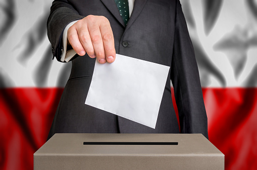 Election in Poland - voting at the ballot box. The hand of man putting his vote in the ballot box. Flag of Poland on background.