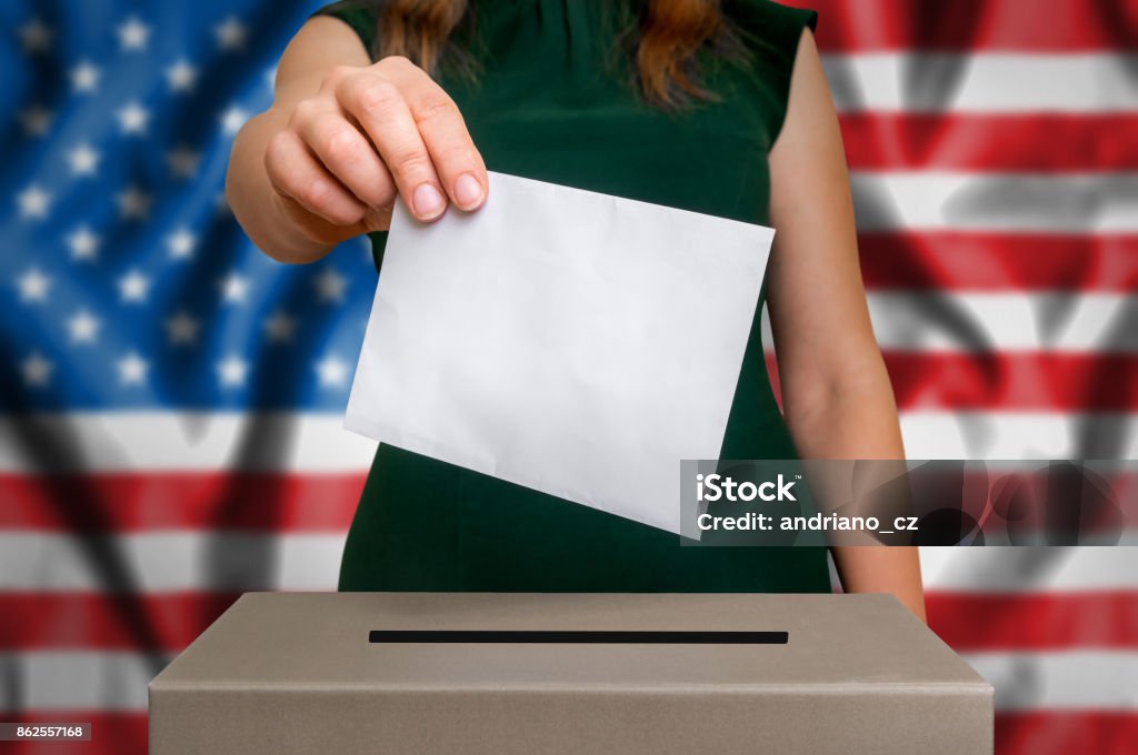 Election in USA - voting at the ballot box Election in United States of America - voting at the ballot box. The hand of woman putting her vote in the ballot box. Flag of USA on background. Voting Stock Photo