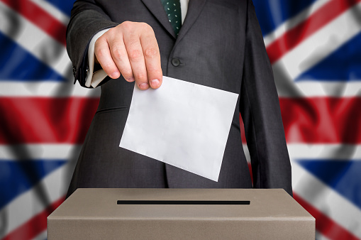 Election in United Kingdom - voting at the ballot box. The hand of man putting his vote in the ballot box. Flag of United Kingdom on background.