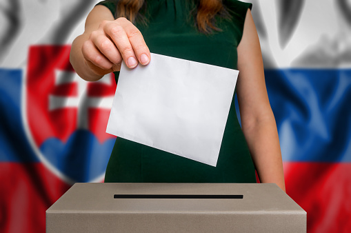 Election in Slovakia - voting at the ballot box. The hand of woman putting her vote in the ballot box. Flag of Slovakia on background.