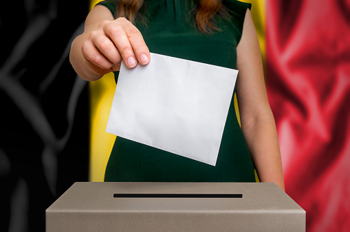 Election in Belgium - voting at the ballot box. The hand of woman putting her vote in the ballot box. Flag of Belgium on background.