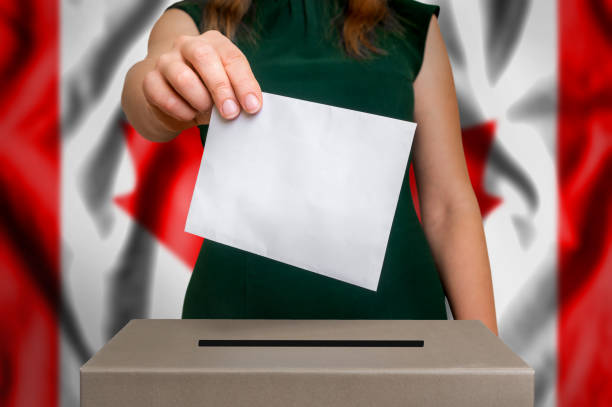 Election in Canada - voting at the ballot box Election in Canada - voting at the ballot box. The hand of woman putting her vote in the ballot box. Flag of Canada on background. dnc stock pictures, royalty-free photos & images