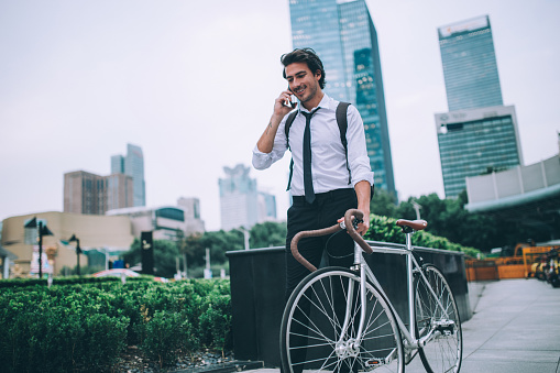 One man, young and handsome standing outdoors next to his bicycle, using smart phone.