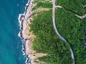 Aerial Top View of the road through Green forest on the mountain on Tropical Island with ocean side. The scenic aerial landscape of nature on a green hill with a road through the wood.