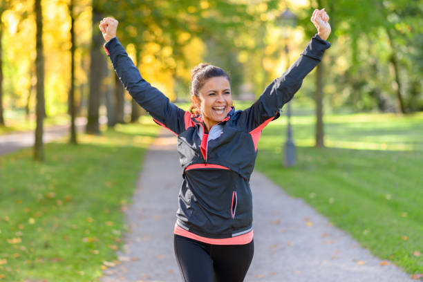 Happy fit woman cheering and celebrating Happy fit middle aged woman cheering and celebrating as she walks along a rural lane through a leafy green park after working out jogging healthy lifestyle women outdoors athlete stock pictures, royalty-free photos & images