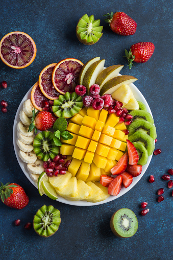 delicious fruits and berries platter on dark blue background. Mango, kiwi, pineapple, banana, blood orange, pear, strawberry, raspberry, pomegranate. top view.