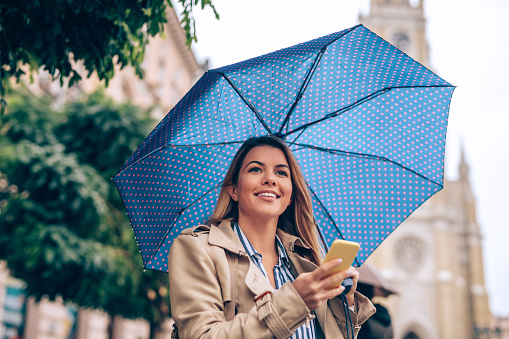 Young woman holding an umbrella and using mobile phone in the city.