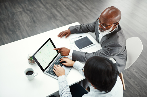 High angle shot of two colleagues using a laptop together at a desk in a modern office