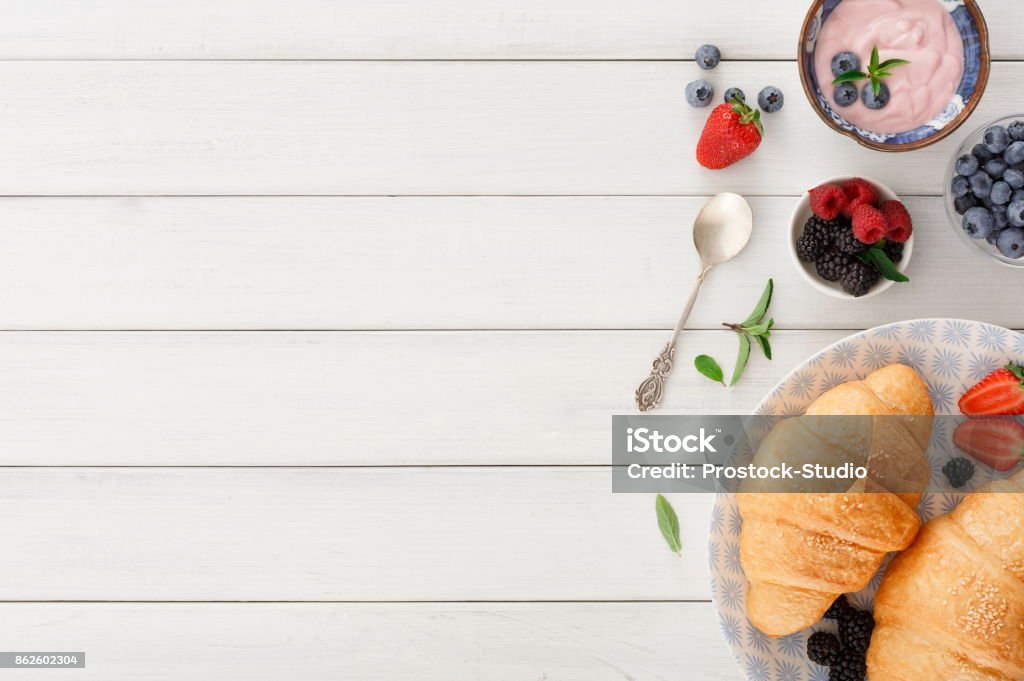 Continental breakfast with croissants and berries on checkered cloth Rich continental breakfast. French crusty croissants, muesli,greek yogurt and lots of sweet berries for tasty morning meals. Delicious start of the day. Top view with copy space on white wood Breakfast Stock Photo