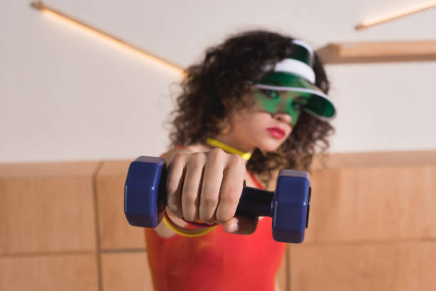 woman in bright cap showing dumbbell in hand selective focus of woman in bright cap showing dumbbell in hand 80s aerobics stock pictures, royalty-free photos & images