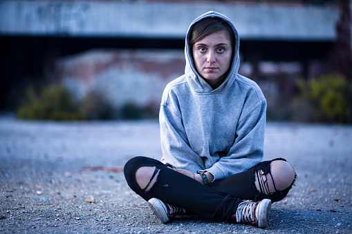 Woman with Sweatshirt and Torn Trousers Sitting on the Street