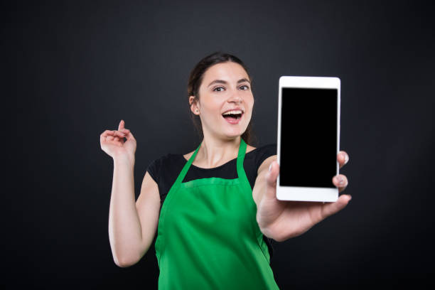 Smiling supermarket female employee showing smartphone stock photo