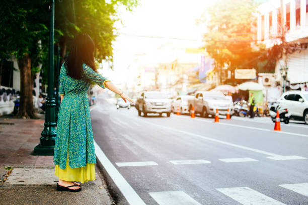 kobieta w tradycyjnej azjatyckiej sukience stojącej na ścieżce machając do usług transportowych, takich jak taksówka lub autobus w bangkoku, tajlandia - krungthep zdjęcia i obrazy z banku zdjęć