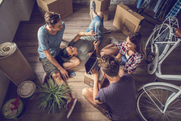 Above view of happy roommates using wireless technology in new apartment. High angle view of relaxed people taking a break from relocating and using wireless technology. roommate stock pictures, royalty-free photos & images