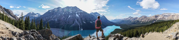 Panoramic of young man hiker on rock above mountain lake