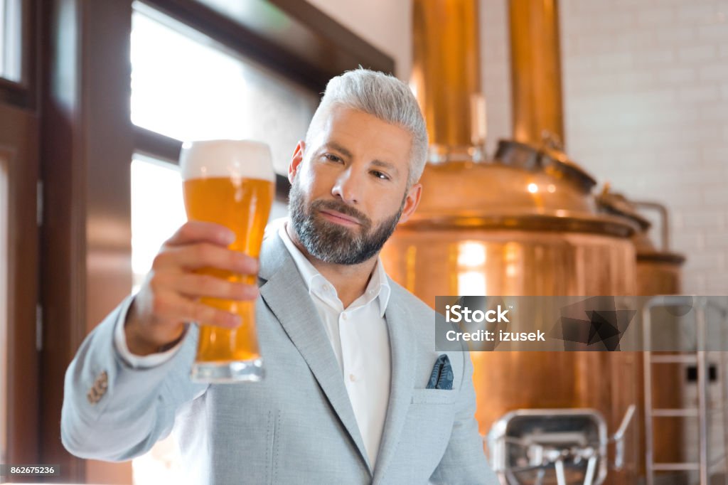 The microbrewery owner holding a beer glass in his pub The microbrewery owner standing in front to copper vat and holding beer glass, checking quality. Beer - Alcohol Stock Photo