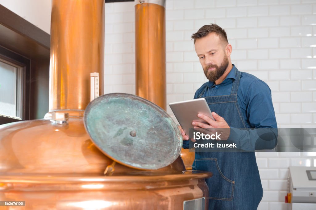 The master brewer using a digital tablet in his micro brewery Master brewer standing next to copper vat and using a digital tablet in his micro brewery. Digital Tablet Stock Photo