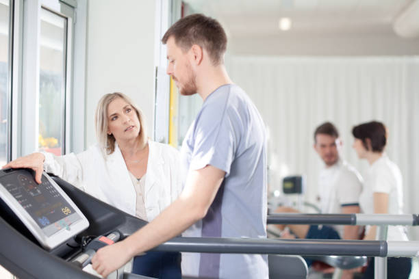 athlète sur un tapis roulant avec médecin physiothérapeute - centre de désintoxication photos et images de collection