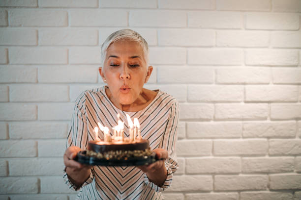 Make a wish! A beautiful senior lady making a wish and blowing candles on her lovely birthday cake. woman birthday cake stock pictures, royalty-free photos & images