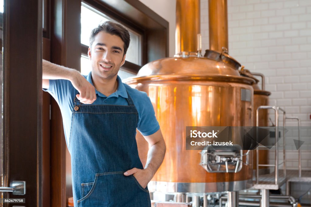 The master brewer in micro brewery Happy master brewer standing in front to copper vat and smiling at the camera. Apron Stock Photo