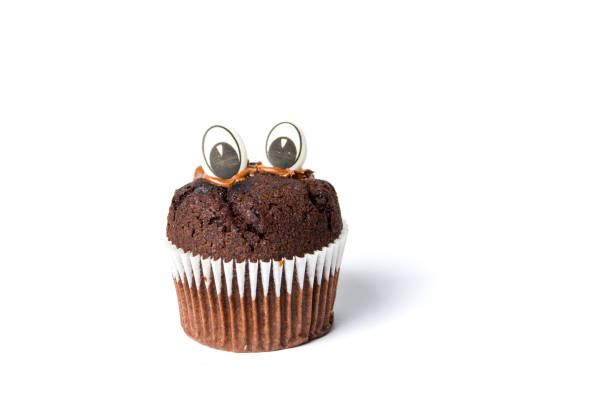 Chocolate muffin with edible eyes in paper holder on white