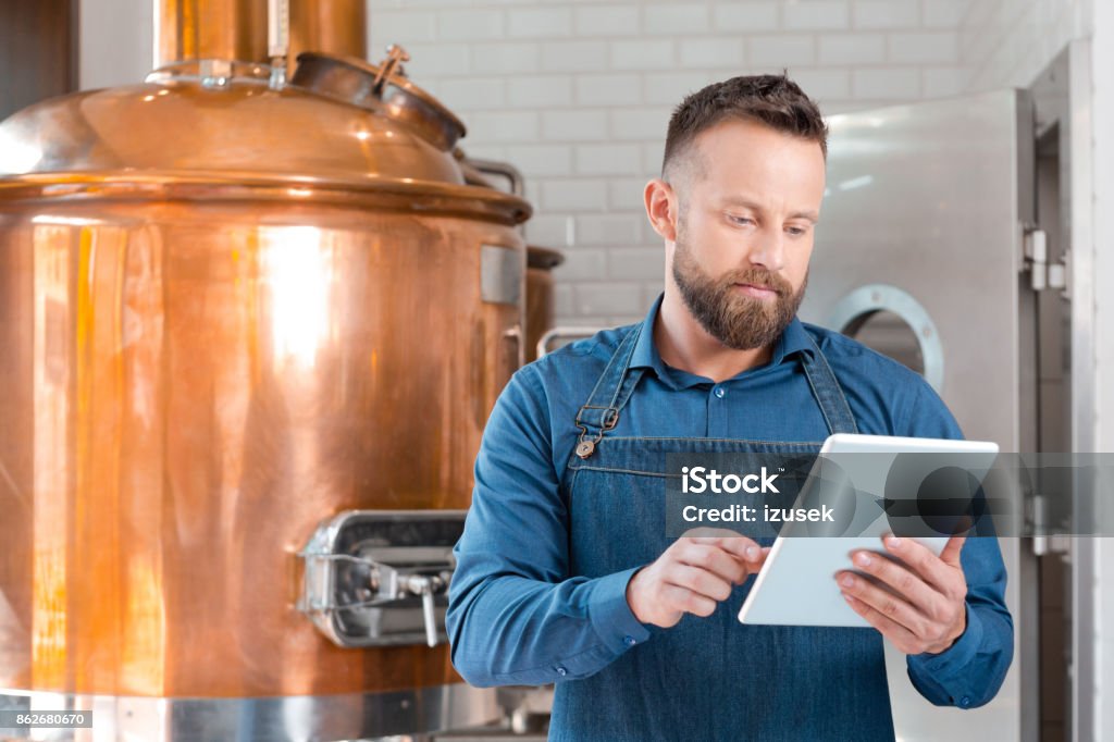 The master brewer using a digital tablet in his micro brewery Master brewer standing in front to copper vat and using a digital tablet in his micro brewery. Brewery Stock Photo