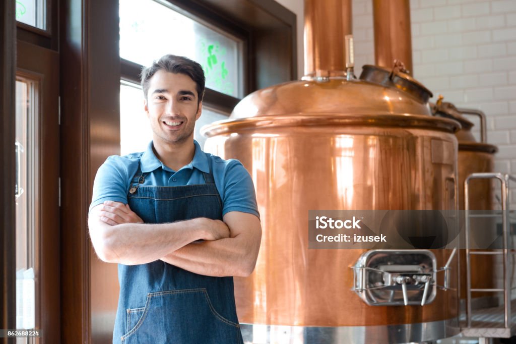 The bartender standing with crossed arms in microbrewery Happy bartender standing in front to copper vat and smiling at the camera. Beer - Alcohol Stock Photo