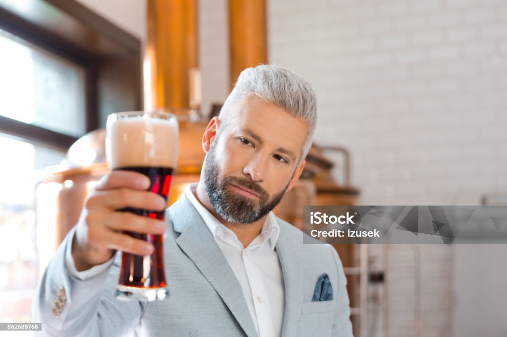 The microbrewery owner holding a beer glass in pub Confident microbrewery owner standing in front to copper vat and holding beer glass. Adult Stock Photo