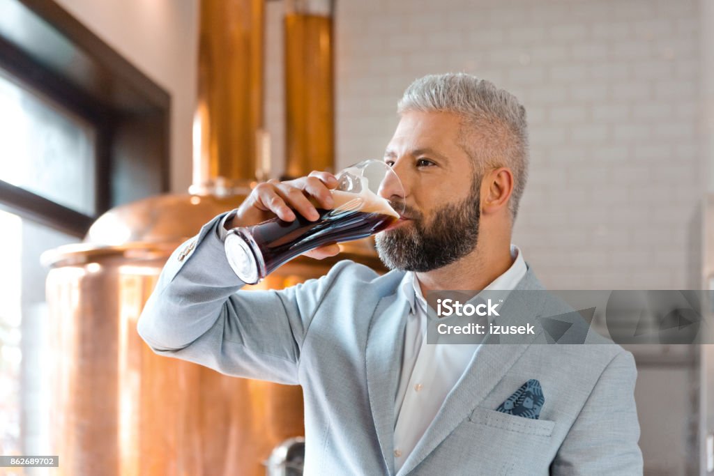 The microbrewery owner drinking ale beer in his pub The microbrewery owner standing in front to copper vat and drinking ale beer. Adult Stock Photo