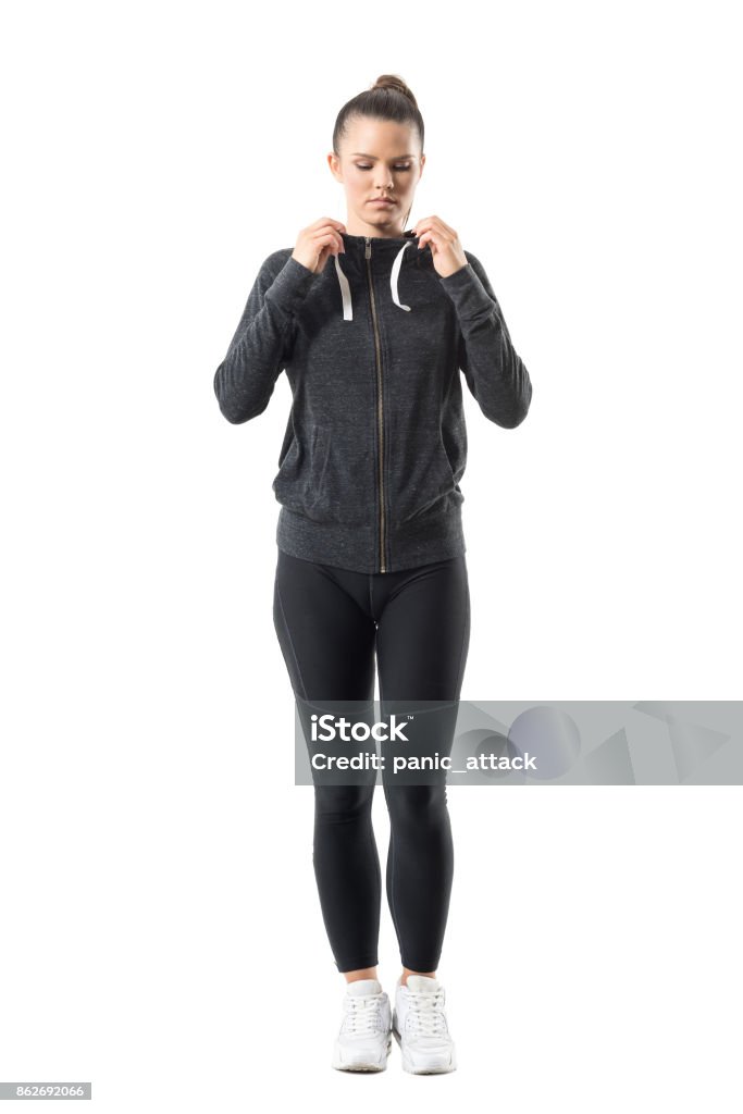 Woman runner in zip up hoodie sweatshirt get ready for running looking down Woman runner in zip up hoodie sweatshirt get ready for running looking down. Full body length portrait isolated on white background. Athlete Stock Photo