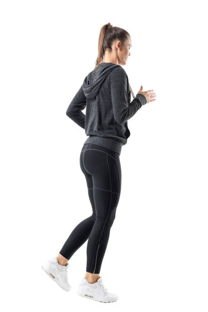 Rear side view of sporty female jogger jogging in hooded sweatshirt and leggings Rear side view of sporty female jogger jogging in hooded sweatshirt and leggings. Full body length portrait isolated on white background. yoga pants stock pictures, royalty-free photos & images