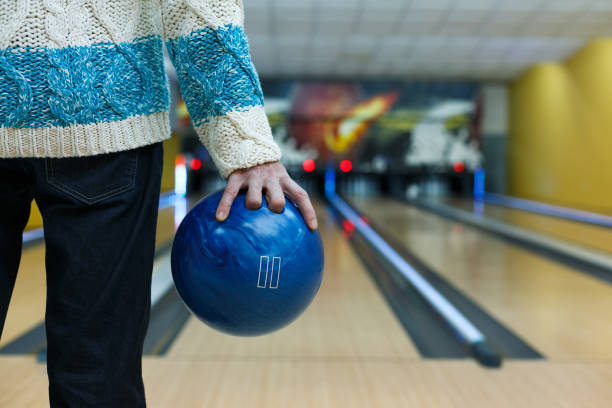 Man holds ball at bowling lane, cropped image Unrecognizable man holds ball, prepare to throw it to bowling lane, closeup. Player plays active game. Cropped image of male leisure bowling alley wood stock pictures, royalty-free photos & images