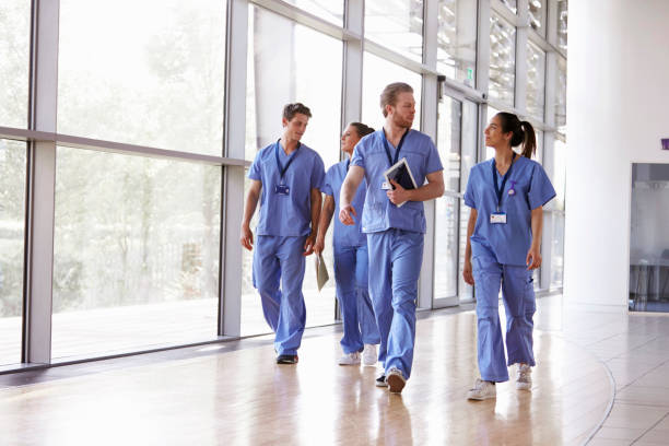 four healthcare workers in scrubs walking in corridor - medical occupation imagens e fotografias de stock