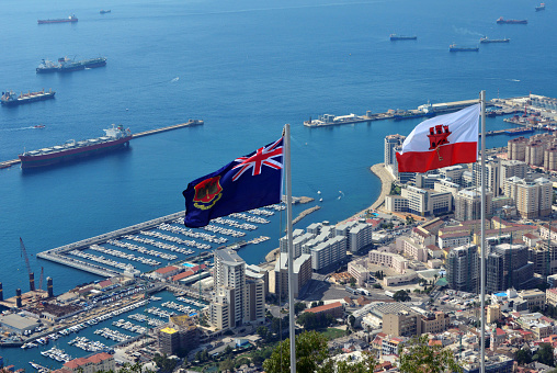 Gibraltar: flag of Gibraltar and the Government Ensign - seen against the Bay of Algerciras with the port, reclamation areas and the town on the lower right - photo by M.Torres