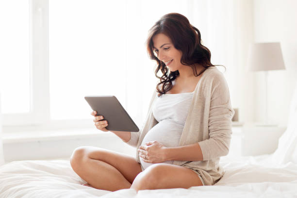 femme enceinte heureuse avec tablet pc à la maison - using computer bedroom one woman only cheerful photos et images de collection