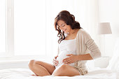 happy pregnant woman sitting on bed at home
