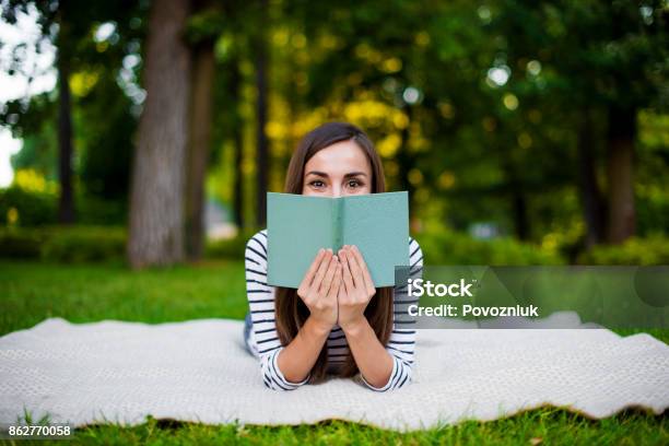 Beautiful Smiling Modern Young Girl Student In Casual Clothes Reading A Book Lying On A Plaid In A City Park Stock Photo - Download Image Now