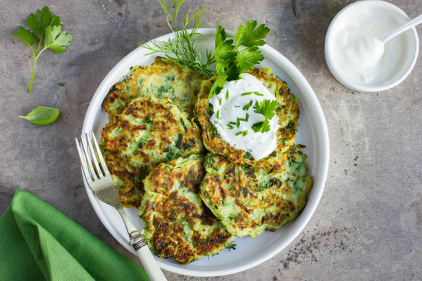 zucchini fritters, vegetarian zucchini pancakes, served with fresh herbs and garlic yogurt sauce zucchini fritters, vegetarian zucchini pancakes, served with fresh herbs and garlic yogurt sauce, top view fritter photos stock pictures, royalty-free photos & images