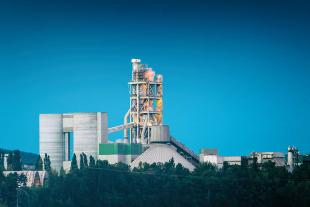 French cement factory industrial building on riverbank at twilight time of the day on blue sky blue hour Horizontal composition cold colors photography of exterior of factory, industrial building at water's edge and at twilight time of the day, blue hour, with dark blue clear sky with copy space. This is a cement factory, concrete industry manufacturing. This picture was taken in Montalieu-Vercieu town, in Isere, in Auvergne-Rhone-Alpes region in France (Europe), along the Rhone river. cement factory stock pictures, royalty-free photos & images