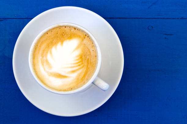 istock Cappuccino in white ceramic cup with saucer on blue painted wood from above. 862959582